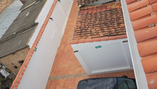 Un'auto nera parcheggiata su un tetto piastrellato, un muro bianco con un cartello verde e un muro in mattoni con un tetto in tegole.