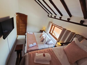 Un dormitorio con dos camas, televisión, armario de madera y ventana con cortinas.