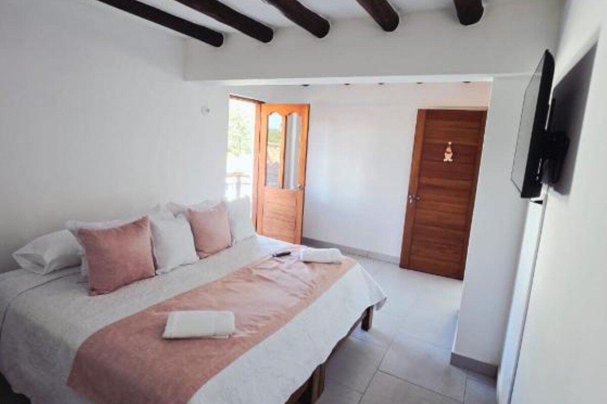 Un dormitorio con cama, una puerta de madera y un televisor montado en la pared.