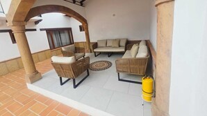 Un'area patio riparata con mobili in vimini, una bombola di gas gialla e pavimento piastrellato.