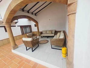 A covered patio area with wicker furniture, a yellow gas cylinder, and a tiled floor. - Casa Hotel La Morada (Villa de Leyva)