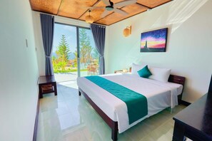 A hotel room with a bed, a desk, a chair, a ceiling fan, and a view of the outdoors. - Adora Bay Ke Ga Beach Resort (Tan Thanh)