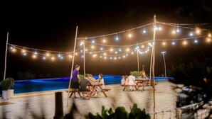 An outdoor dining area with string lights, wooden tables, and a pool in the background. - Adora Bay Ke Ga Beach Resort (Tan Thanh)