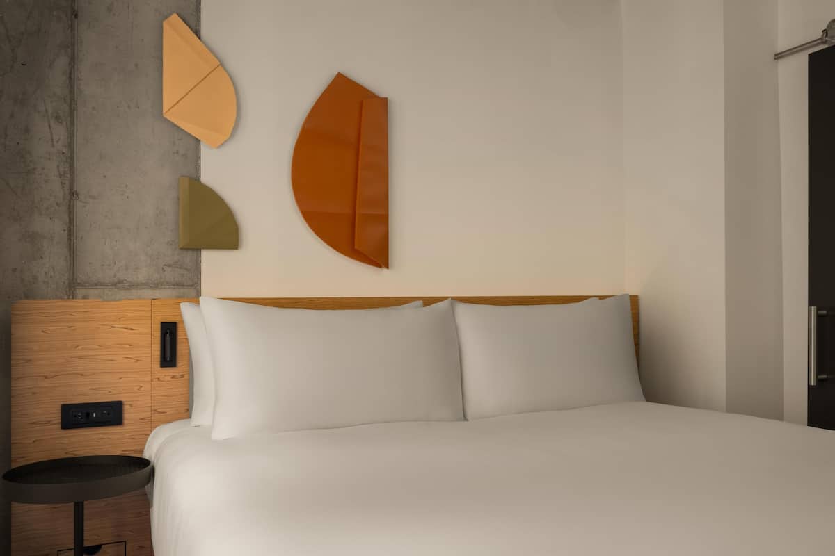 Una cama con ropa blanca, un cabecero de madera y una mesita de noche con una lámpara.