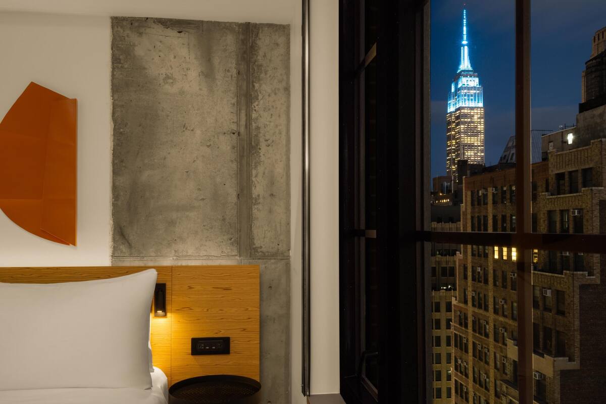 Habitación de hotel con cama, una mesita redonda, un muro decorativo de madera y vistas del Empire State Building.
