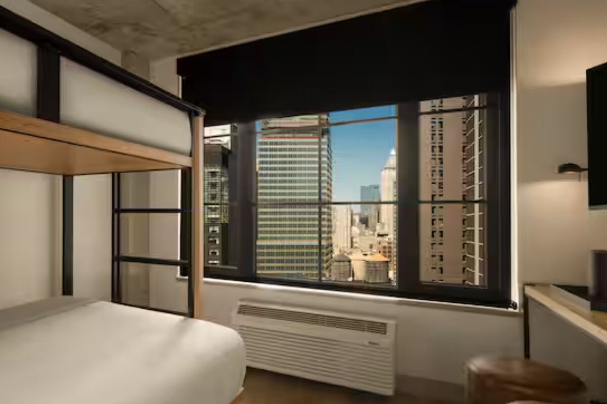 Un dormitorio moderno con una cama litera, un ventanal con vista a la ciudad y un radiador.