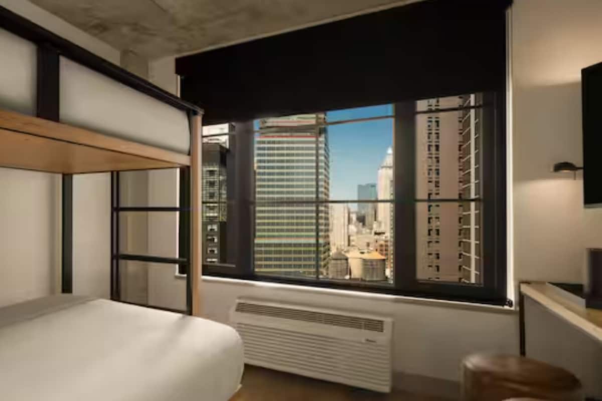 Un dormitorio moderno con una cama litera, un ventanal con vista a la ciudad y un radiador.