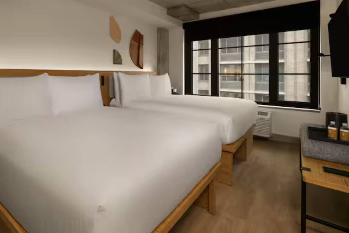 Habitación de hotel con una cama grande, mesitas de noche, un escritorio y una ventana con persianas.