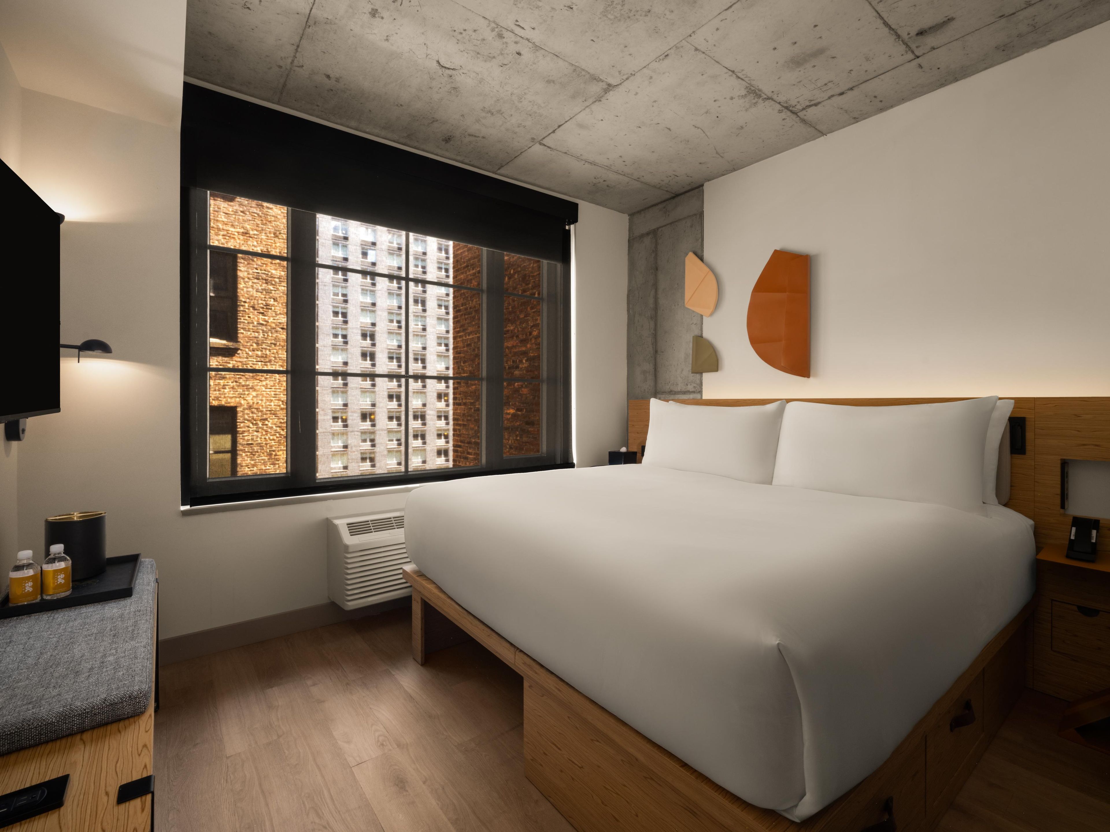 Quarto de hotel moderno com uma cama grande, uma mesa pequena, um aquecedor e uma janela com vista para a cidade.