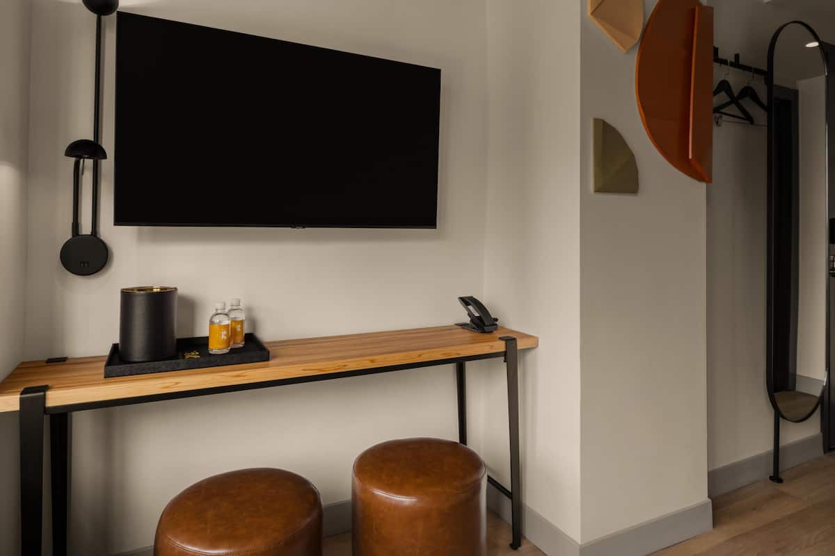 Una habitación moderna con una televisión de pantalla plana montada en la pared, un escritorio de madera con teléfono y dos taburetes de cuero.