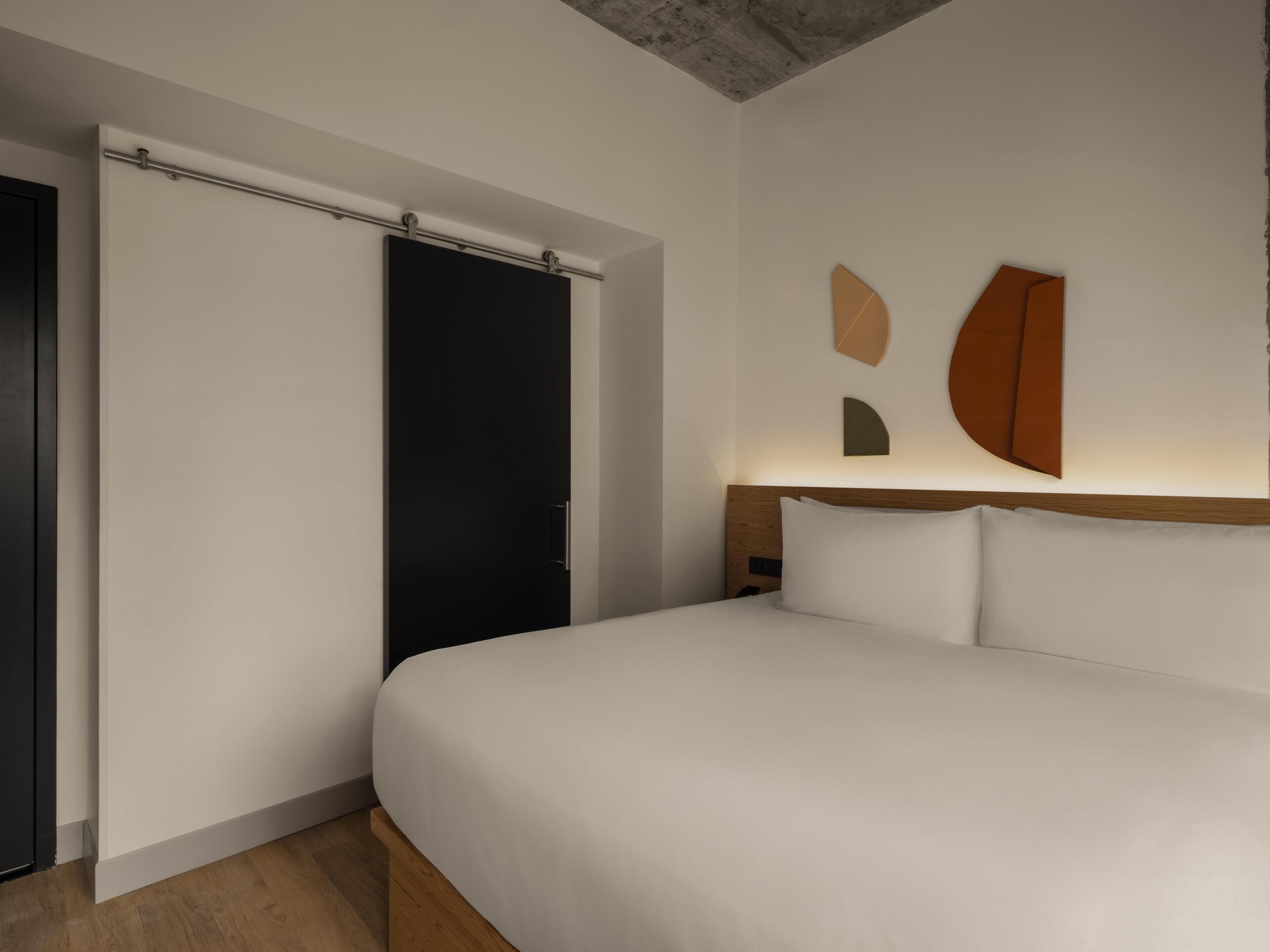 Una habitación de hotel moderna con una cama grande, una puerta corredera y arte abstracto en la pared.