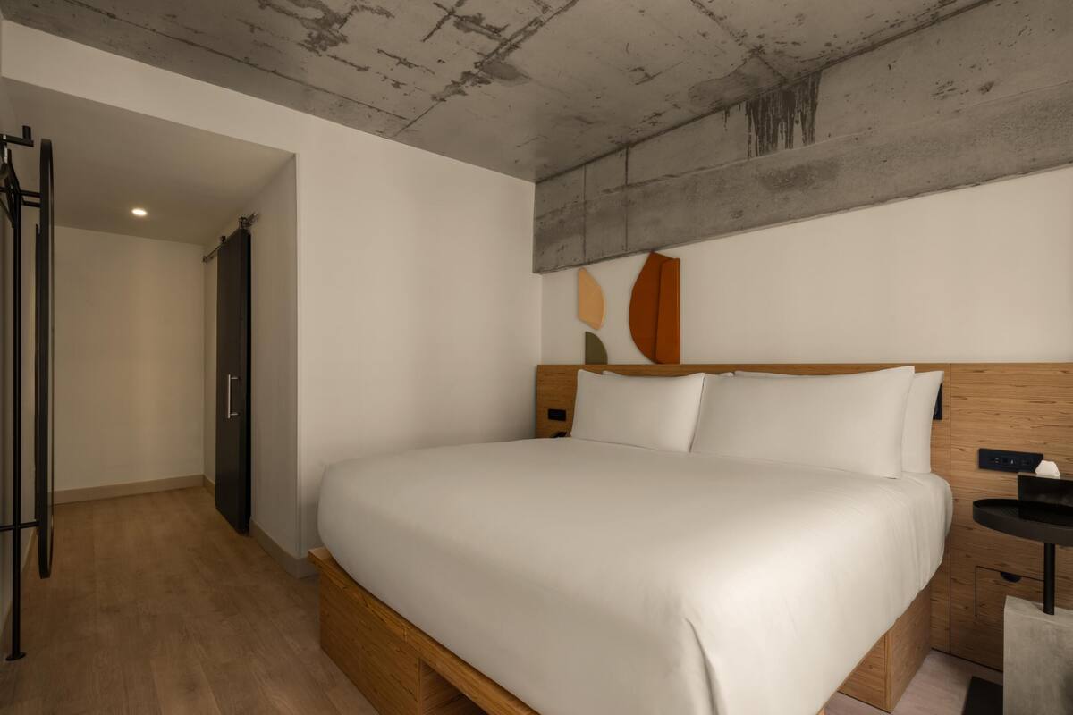 Una habitación de hotel moderna con una cama de madera, una mesita de noche pequeña y un armario.
