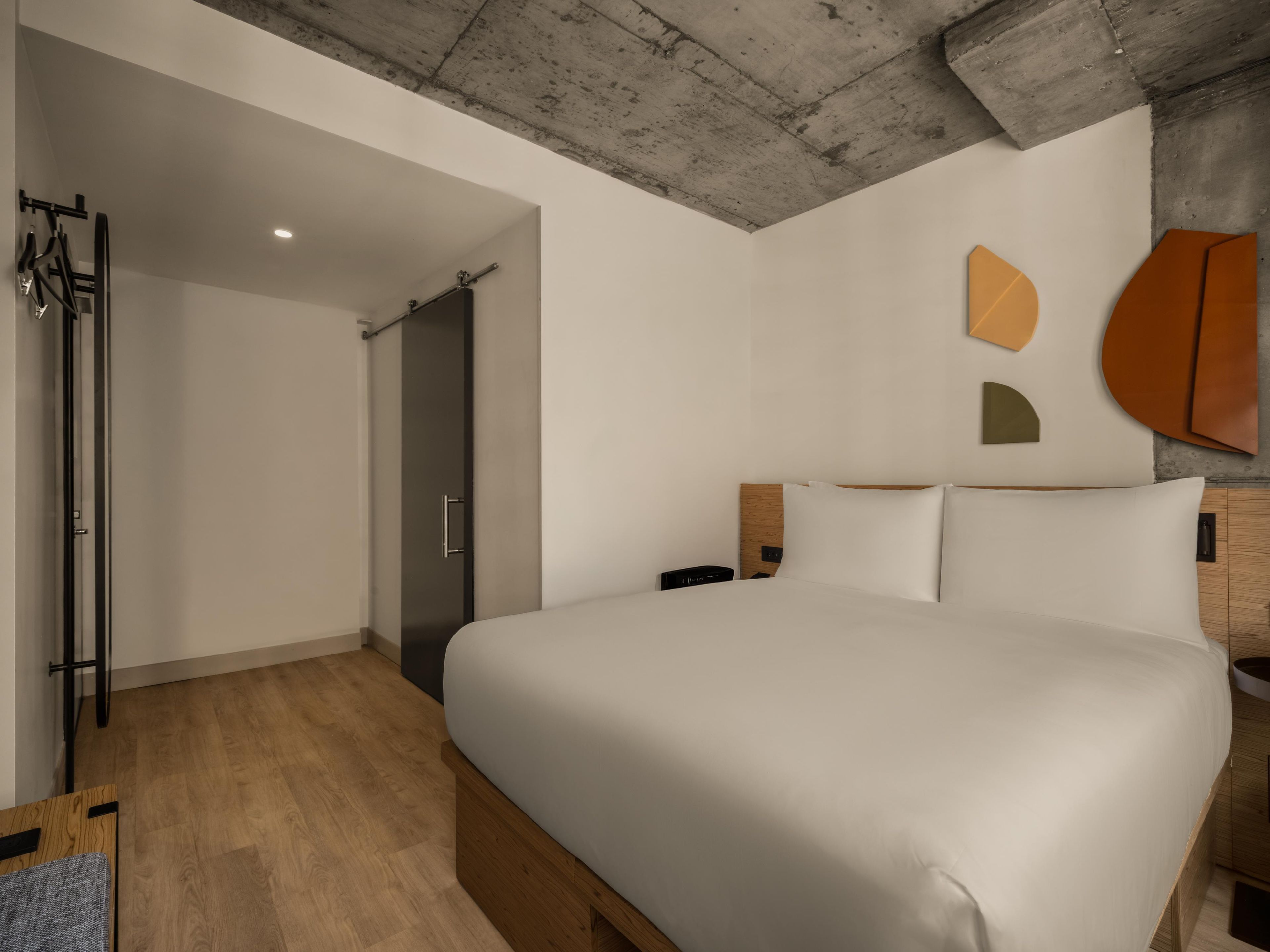 Una habitación de hotel moderna con una cama grande, suelo de madera, techo de hormigón y un diseño minimalista.