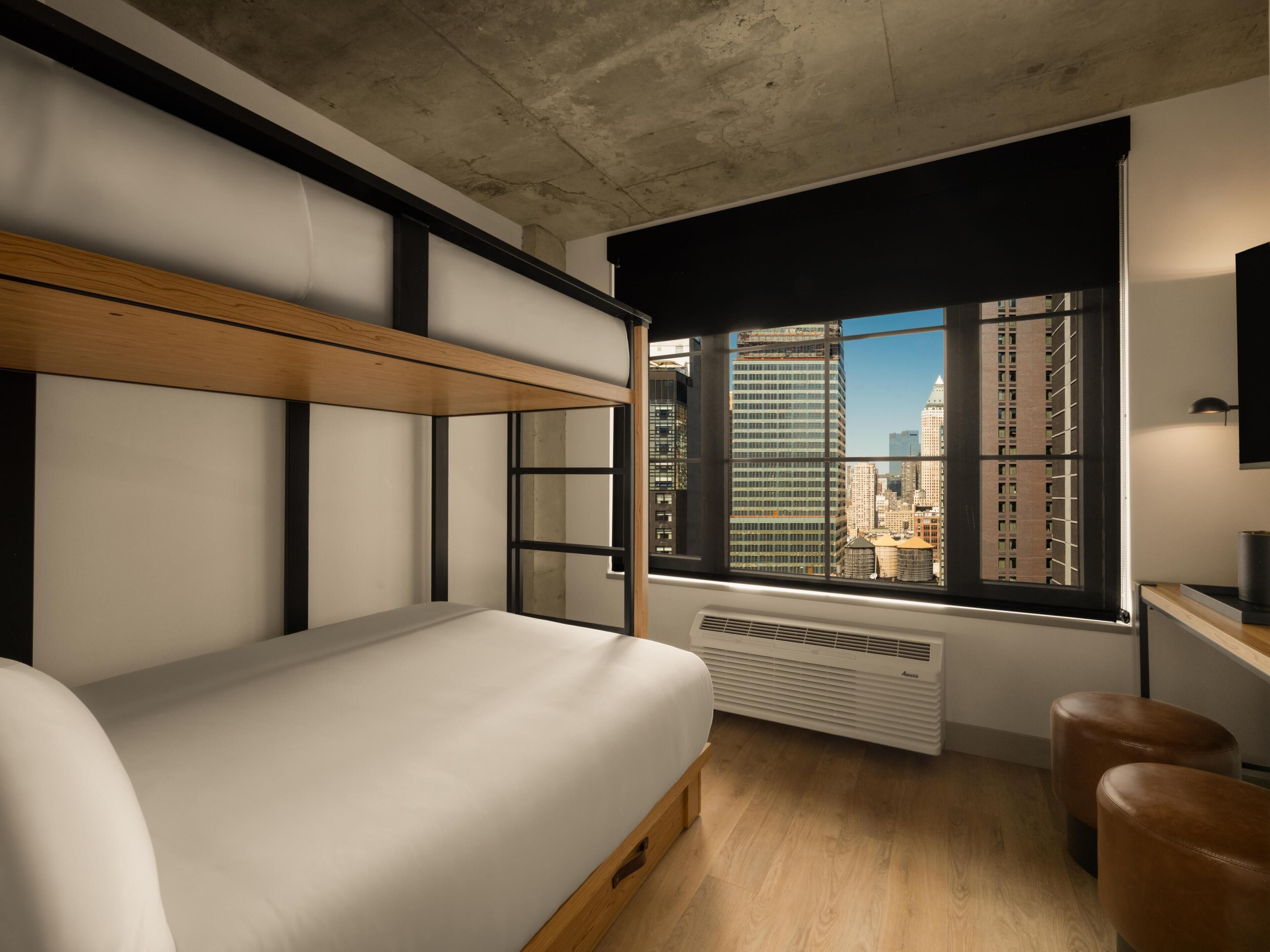 Una habitación moderna con una litera, un escritorio, una silla y un ventanal con vistas a la ciudad.