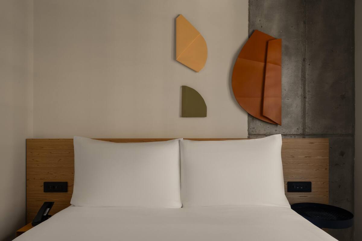 Una cama con sábanas blancas, cabecera de madera y una pared con obras de arte abstracto.