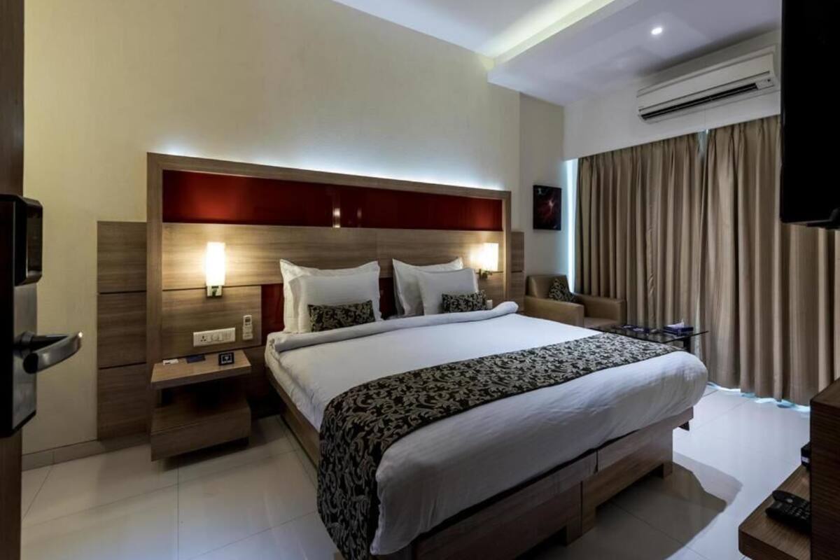 A modern hotel room with a large bed, bedside tables, an air conditioning unit, and a television.