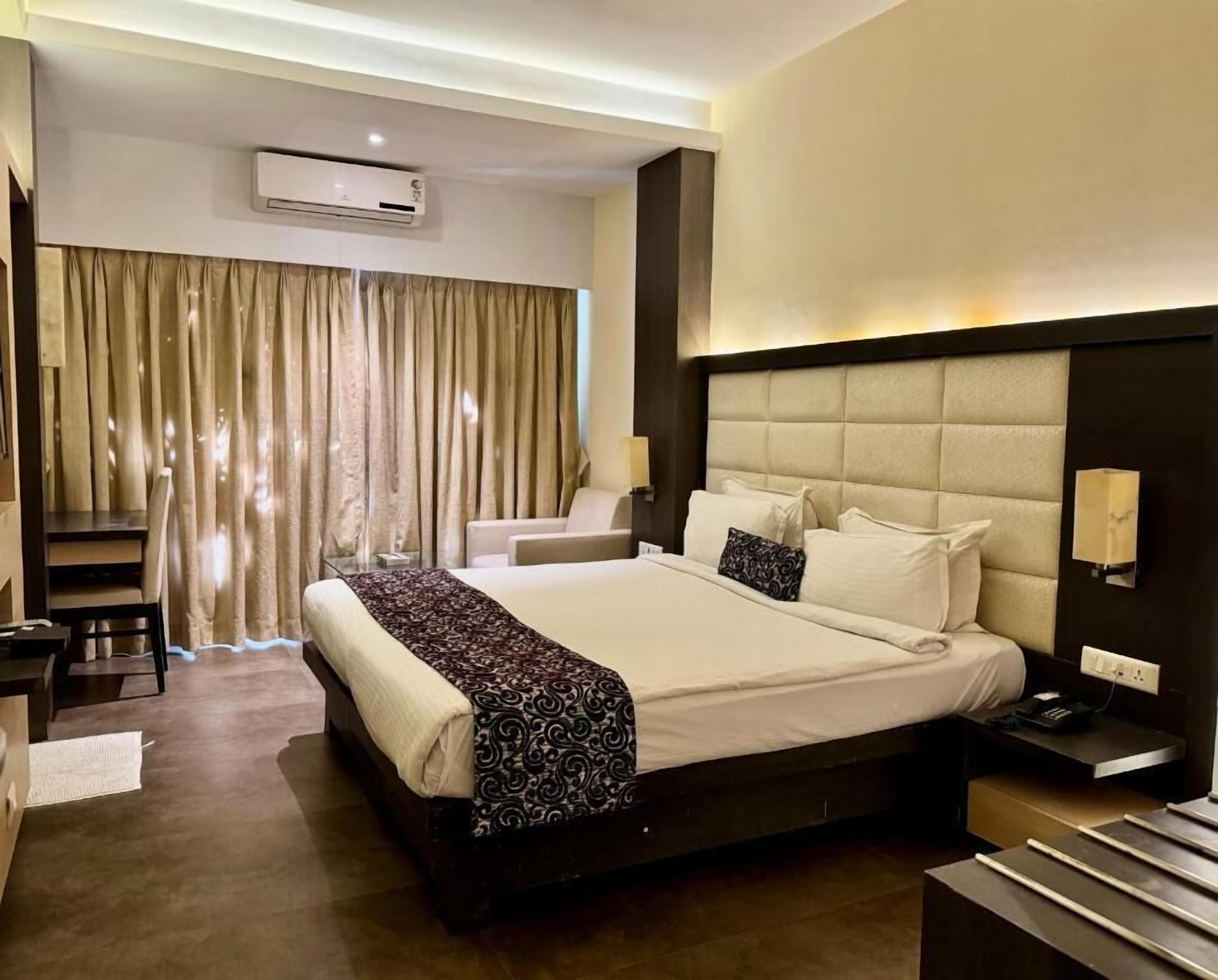 Ein Hotelzimmer mit einem großen Bett, einem Schreibtisch, einem Sessel, einem Nachttisch und einem Fenster mit Vorhängen.