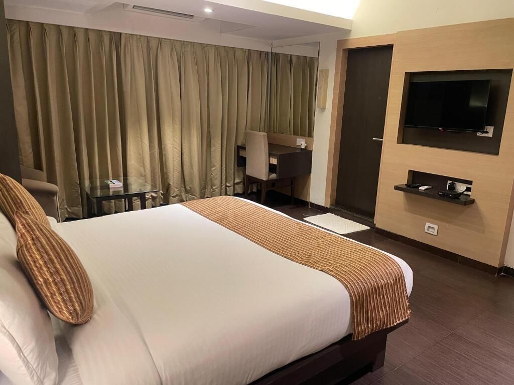 Ein Hotelzimmer mit einem großen Bett, einem Schreibtisch, einem Stuhl, einem an der Wand montierten Fernseher und einer Tür.