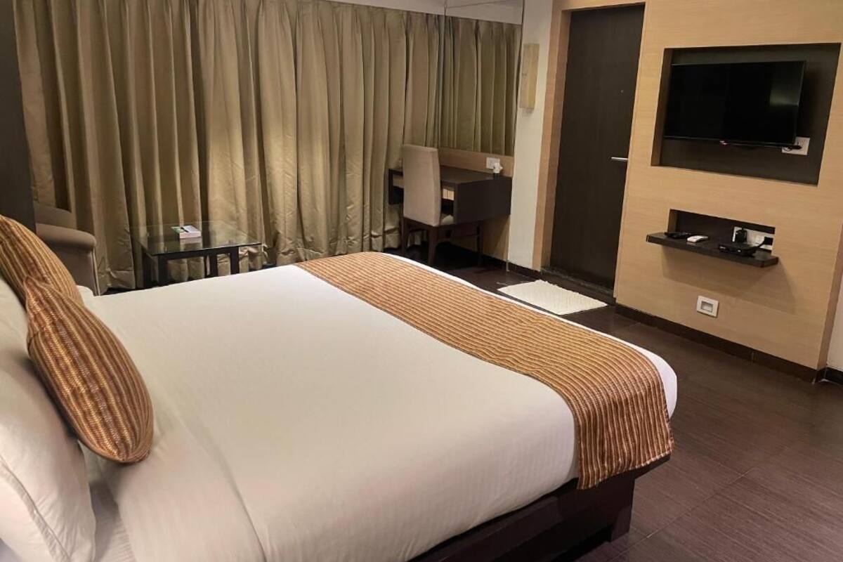 A hotel room with a large bed, a desk, a chair, a television mounted on the wall, and a door.