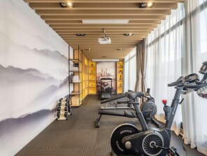 A gym with exercise equipment, a wall with a mountain painting, and a cityscape poster. - Mercure Shanghai Pudong Zhangjiang Park (Zhoushan)