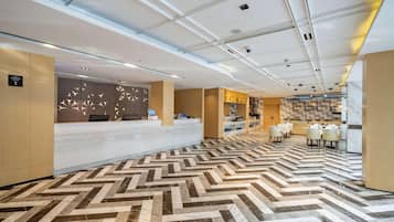 Un moderno vestíbulo de hotel con una recepción, una zona de estar y una cocina a lo lejos.