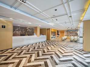 A modern hotel lobby with a reception desk, a seating area, and a kitchen visible in the background. - Mercure Shanghai Pudong Zhangjiang Park (Zhoushan)