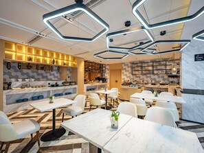 A modern restaurant with marble flooring, white tables, and chairs. There are hexagonal ceiling lights and a kitchen area with a buffet. - Mercure Shanghai Pudong Zhangjiang Park (Zhoushan)