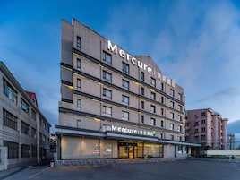 Un hotel de varios pisos con un diseño moderno, que destaca un letrero grande de 'Mercure' en la fachada.