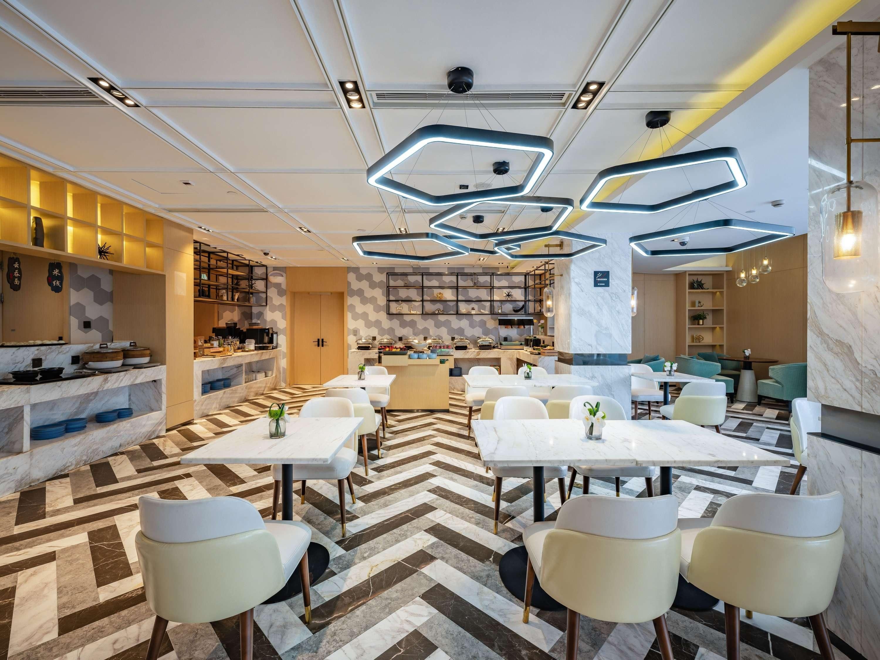 A modern dining area with marble flooring, white tables, and chairs, and a kitchen in the background.