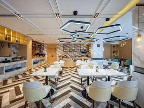 A modern dining area with marble flooring, white tables, and chairs, and a kitchen in the background.