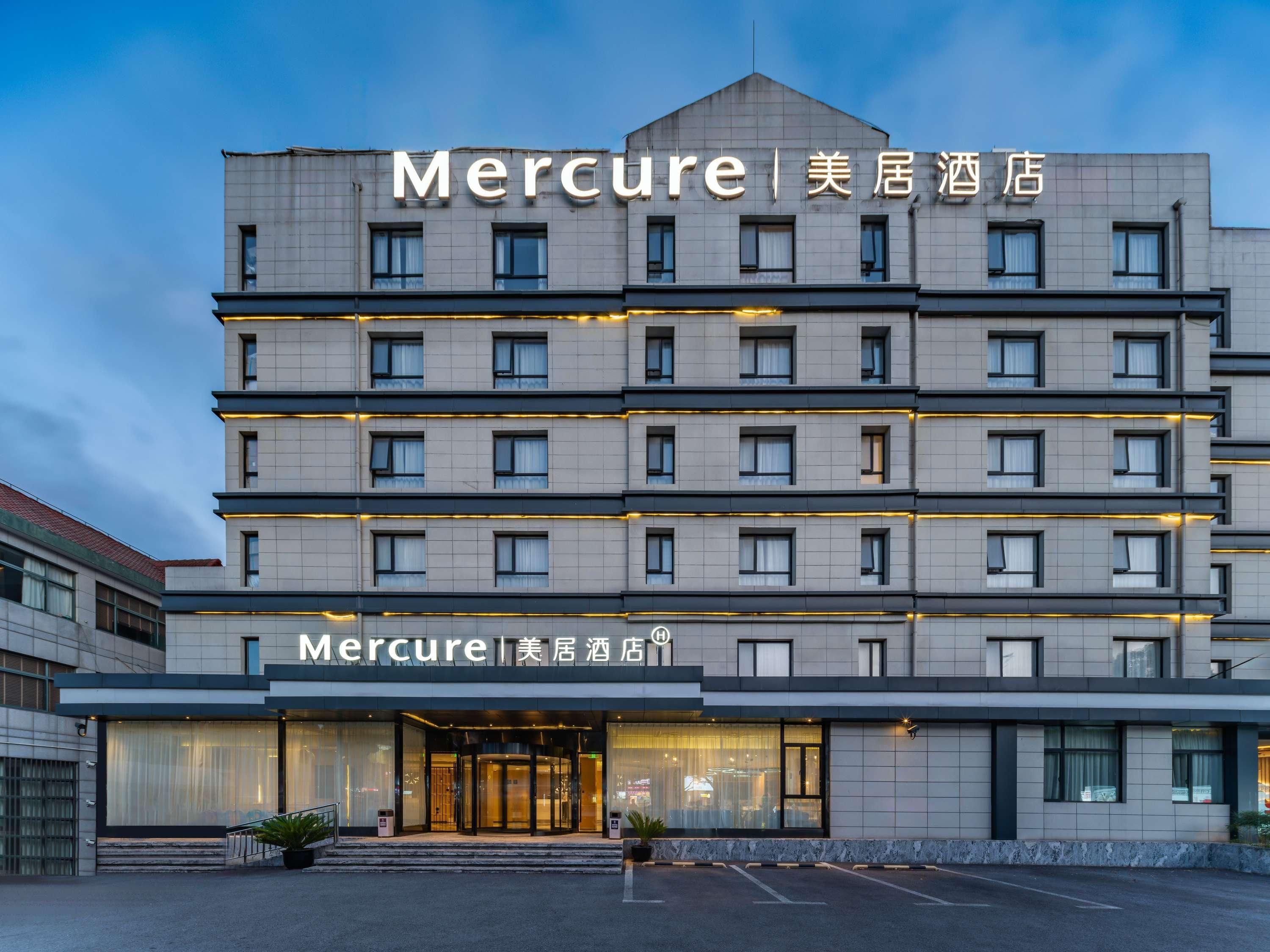 A multi-story hotel with a modern facade, featuring a prominent entrance with glass doors and a visible parking area in front.