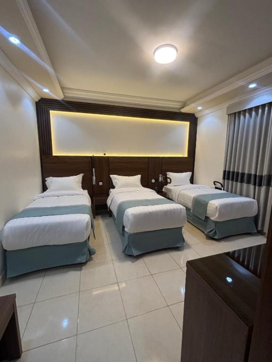 A hotel room with three beds arranged in a row, a large illuminated panel above the headboard, and a modern design.