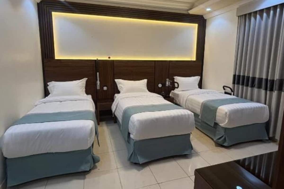 A hotel room with three beds arranged in a row, a large illuminated panel above the headboard, and a modern design.