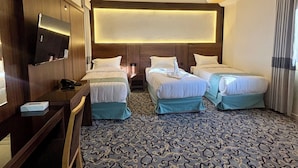 Habitación de hotel con dos camas, un escritorio, un televisor y una alfombra estampada.