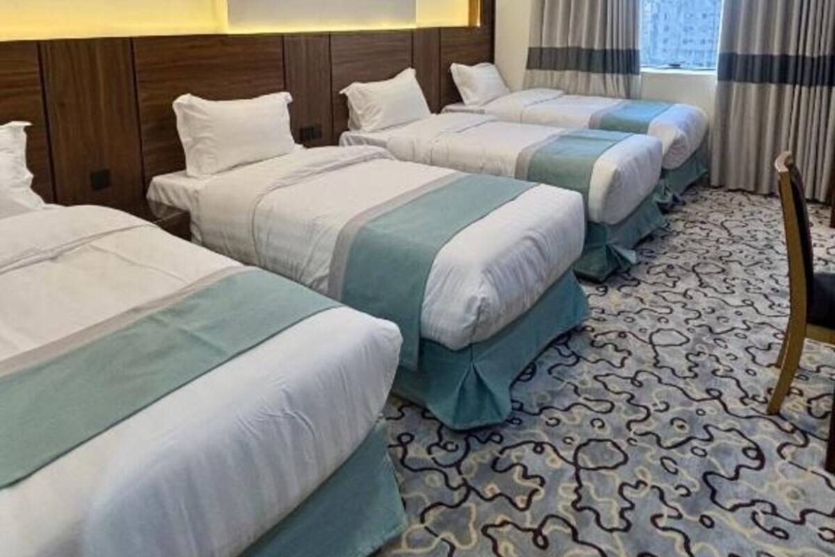 A hotel room with four beds, a patterned carpet, a wooden headboard, and a window with curtains.
