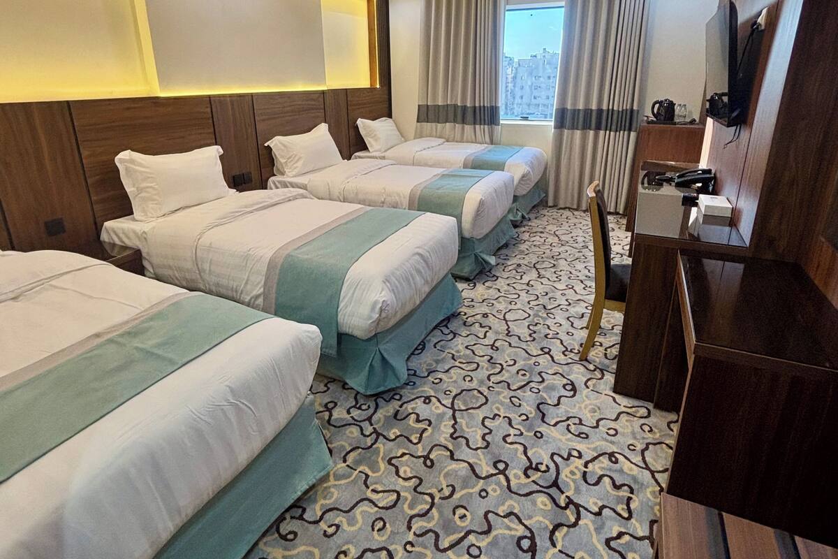 A hotel room with three beds, a desk, a television, and a window with curtains.
