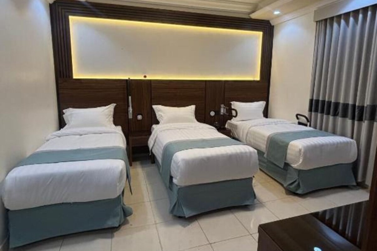 Een hotelkamer met drie bedden op rij, een groot verlicht paneel boven het hoofdeinde en een modern ontwerp.