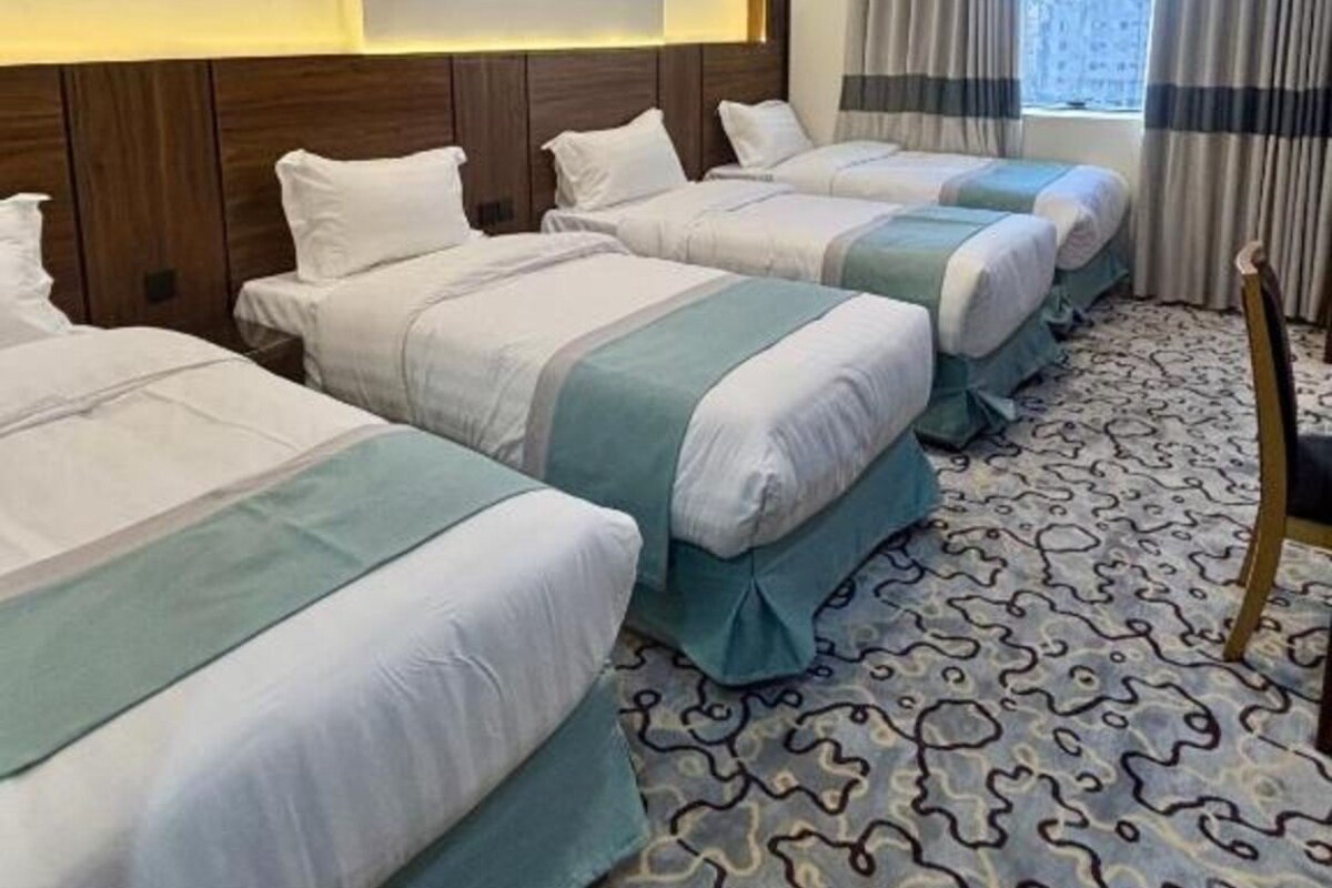 Een hotelkamer met vier bedden, een kamerbreed tapijt met dessin, een houten hoofdeinde en een raam met gordijnen.
