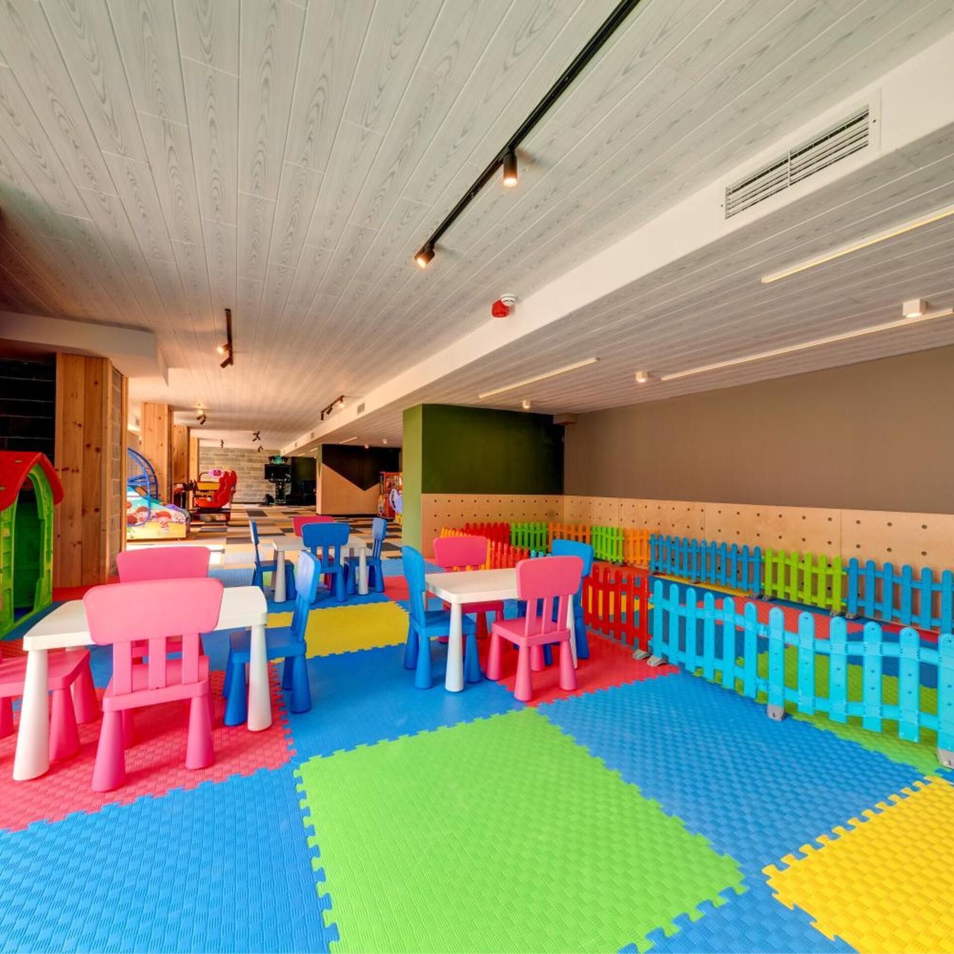 Un área de juegos infantiles con mesas, sillas y alfombras de colores.