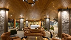 A lobby with a wooden ceiling, stone walls, a central seating area with a sofa and chairs, and a checkered coffee table. - Grand Hotel Therme (Razlog)