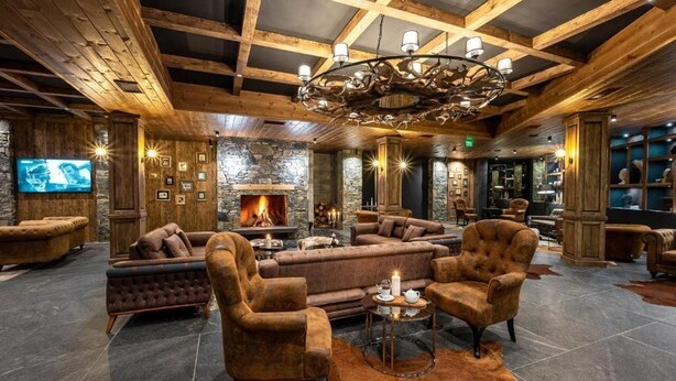 A cozy lounge area with a fireplace, plush seating, and a stone wall backdrop. - Grand Hotel Therme (Razlog)