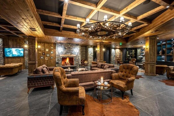 A cozy lounge area with a fireplace, plush seating, and a stone wall backdrop. - Grand Hotel Therme (Razlog)