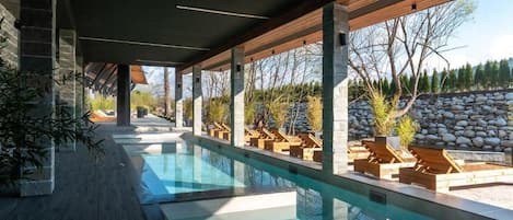 A modern outdoor pool area with lounge chairs and a stone wall backdrop.