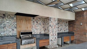 A modern kitchen with a built-in grill, wooden cabinets, and patterned tile walls. - Trigales l Spacious 2BR Home in Las Condes (Santiago)