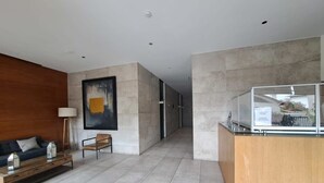 A modern lobby with a wooden reception desk, a sofa, and a painting on the wall. - Trigales l Spacious 2BR Home in Las Condes (Santiago)
