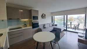 A modern kitchen with a dining area, a sofa, and a balcony with a city view. - Trigales l Spacious 2BR Home in Las Condes (Santiago)