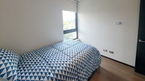 A bedroom with a bed covered in patterned bedding, a window, and a door. - Trigales l Spacious 2BR Home in Las Condes (Santiago)