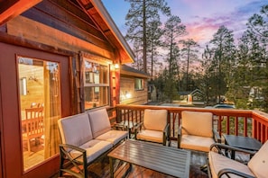 A wooden cabin with a deck, outdoor seating, and a view of a forest. - Sleep11 | Game Cabin + Hot Tub | Near Lake/Village (Big Bear Lake)