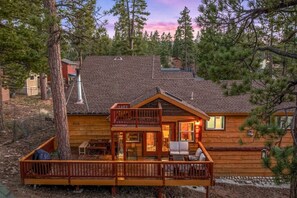 A cabin with a deck, a chimney, and a view of the surrounding forest. - Sleep11 | Game Cabin + Hot Tub | Near Lake/Village (Big Bear Lake)
