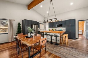 A modern kitchen with dark cabinets, stainless steel appliances, and a wooden dining table. - Sleep11 | Game Cabin + Hot Tub | Near Lake/Village (Big Bear Lake)